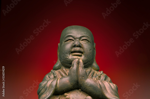 A small replica statue of The Buddha with a red background, red representing luck, joy, and happiness, celebration, vitality, and fertility