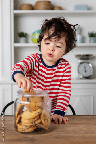 Young boy getting biscuits from cookie jar on kitchen table