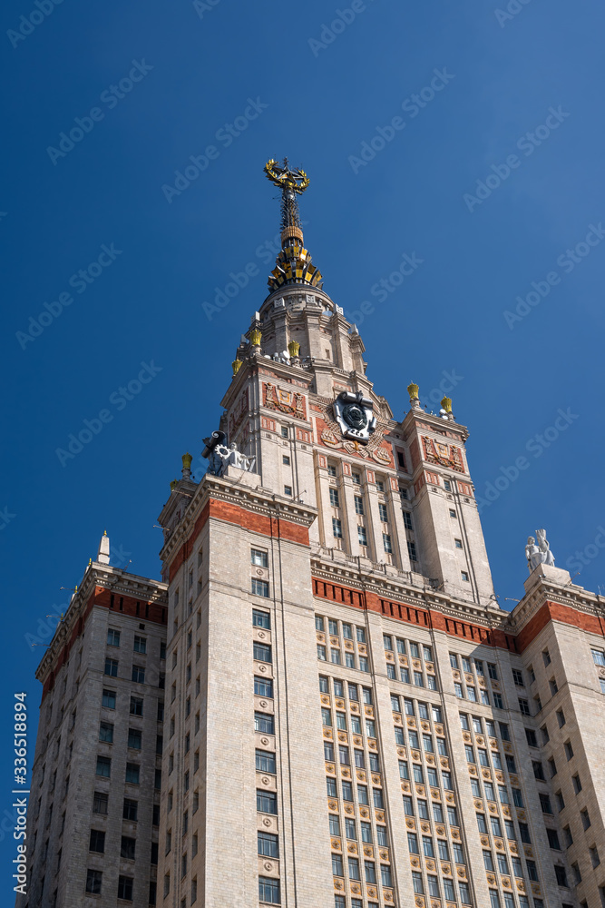 Fragment of a high rise tower in Stalinist monumental architecture style with a gold star and the coat of arms of the USSR on a blue sky background