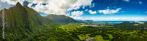 A Panoramic aerial image from the Pali Lookout on the island of Oahu in Hawaii.  With a bright green rainforest, vertical cliffs and vivid blue skies. photo