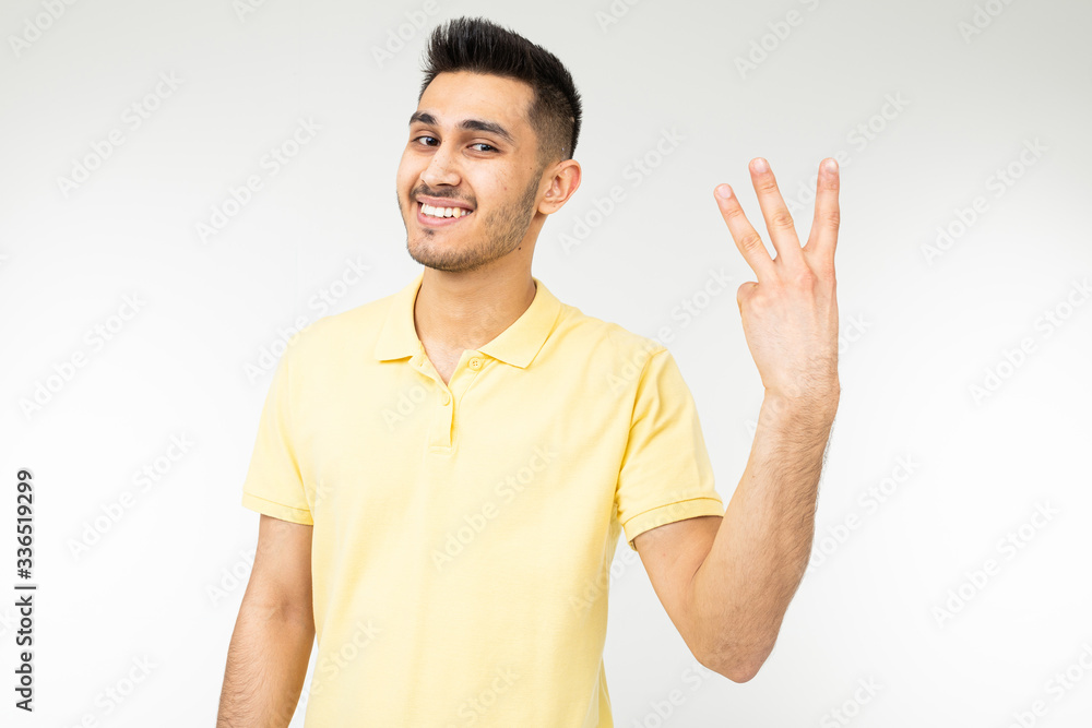Caucasian man in a yellow T-shirt shows three fingers on a white isolated background Caucasian man in a yellow T-shirt shows three fingers on a white isolated background