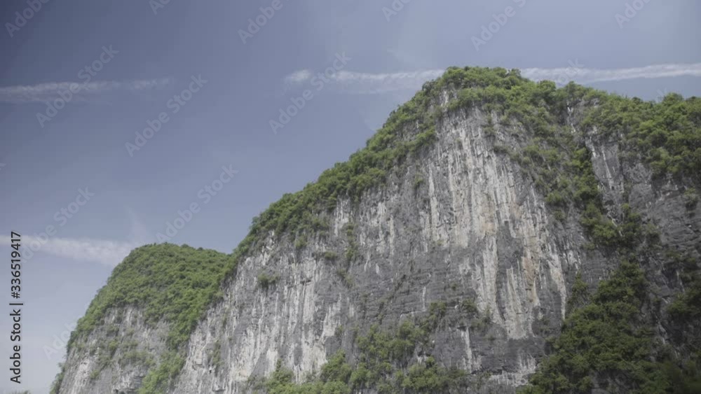 Static shot of a white Chinese mountain dotted with greenery with a blue sky behind