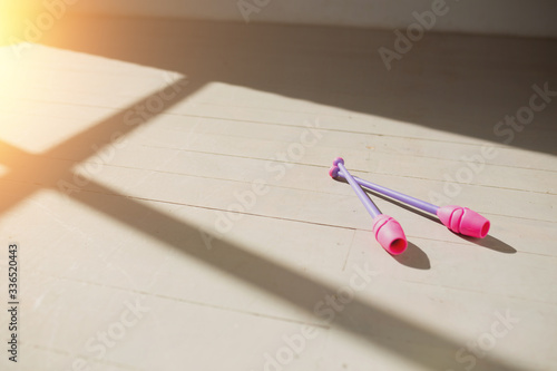 Pink gymnastic wands lying on the wooden floor in the rays of the rising sun. Bright light and shadow.