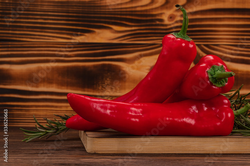 Sweet bell peppers or kapia peppers and rosemary twigs on a cutting board, wooden background with copy space. Fresh vegetables, healthy organic food concept photo