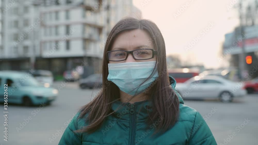A young girl in glasses and a medical mask stands on the street. 4k A young girl in glasses and a medical mask stands on the street. 4k