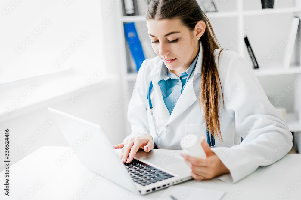 Smiling young female doctor working at the clinic , she is using a computer and writing medical reports. Smiling young female doctor working at the clinic , she is using a computer and writing medical reports.