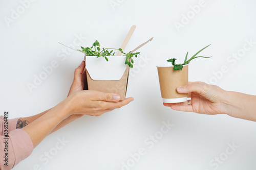 Two people presenting eco friendly containers with greens to each other