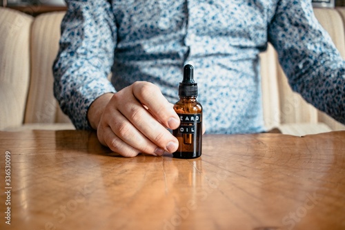 Man holding beard oil on live edge wood table in blue shirt