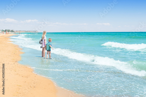 Brother and sister on the beach, the ocean. A teenage girl and a little boy are walking along the coast.