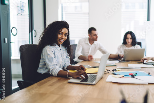 Merry black woman working with laptop during meeting