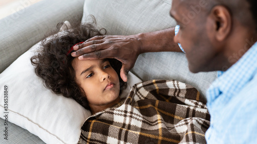 Virus outbreak. Senior African American man touching his granddaughter's forehead, checking fever at home