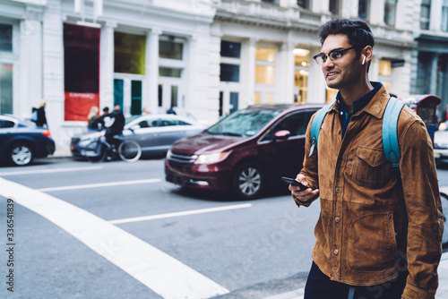 Ethnic young man with phone and headphone walking along street
