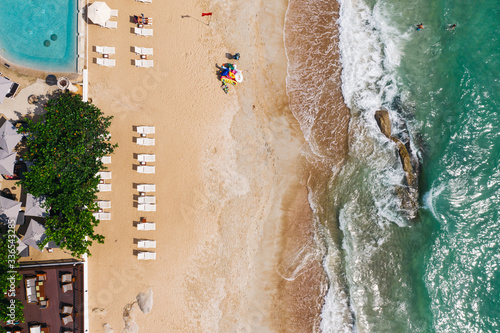 Aerial top view of beachfront hotel resort with sun loungers. Bird's eye tropical view of summer holidays background, turquoise water seashore with umbrellas on clean sand coastline. Paradise rest