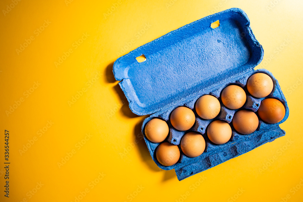 Fresh eggs in blue carton box isolated on yellow background Fresh eggs in blue carton box isolated on yellow background