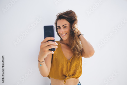 Flirty woman taking selfie picture while stroking hair in sunlight