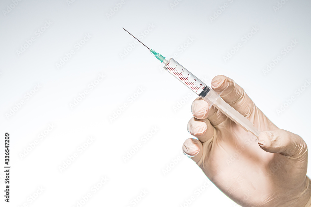 Hand wearing latex glove holding syringe with a medicine on white background Hand wearing latex glove holding syringe with a medicine on white background