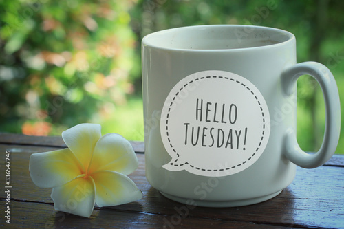 Foto Tuesday greeting welcoming another new day - Hello Tuesday on a white cup of coffee or tea with a flower