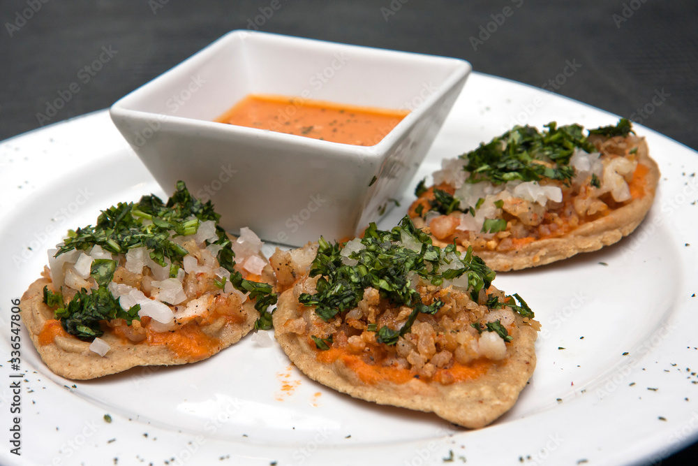 Chalupas con chicharrón de camarón, salsa picante, cilantro y cebolla, comida mexicana, plato blanco sobre fondo negro	