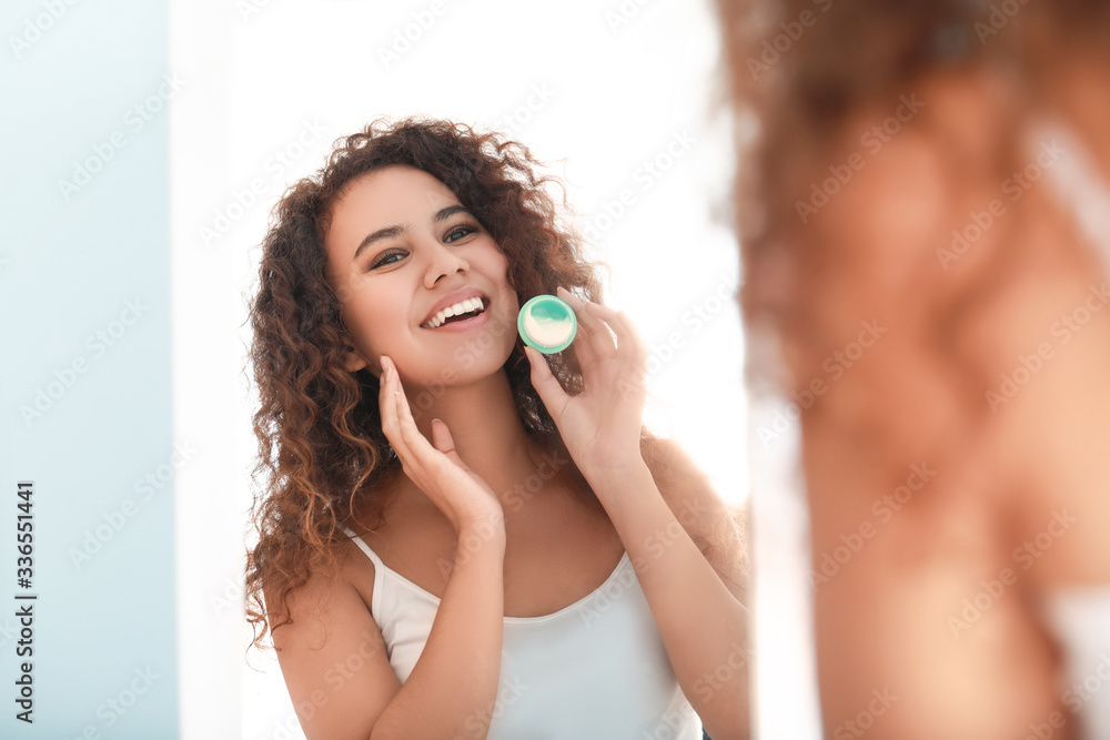 Fototapeta premium Beautiful young African-American woman applying cream at home