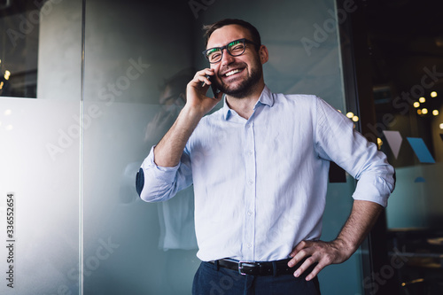 Sincerely man with toothy smile on face enjoying smartphone communication during online phoning in office company, cheerful male banker in optical glasses talking with financial director and laughing © BullRun
