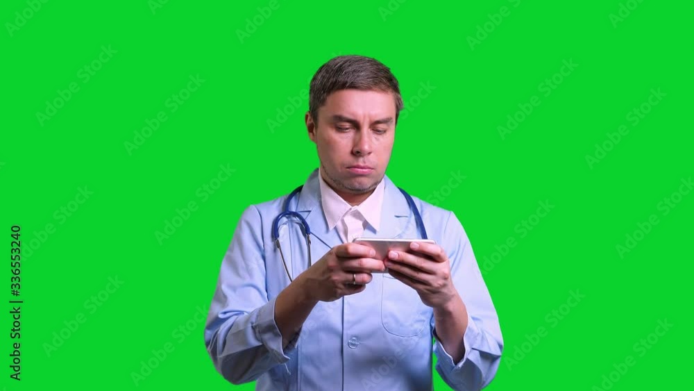 Young doctor using smartphone. Man in blue medical uniform with stethoscope on green chroma key background Young doctor using smartphone. Man in blue medical uniform with stethoscope on green chroma key background