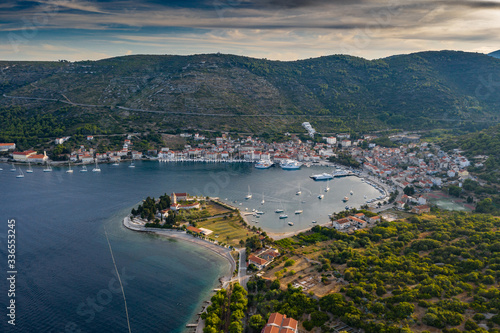 Aerial view of marina Vis at sunset, Croatia, a lot of chaotically standing boats in a bay, roofs of orange color, sunshine, hills with green trees, ferry station