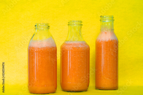 Glass bottles filled with colorful fresh homemade orange, carrot and ginger smoothies