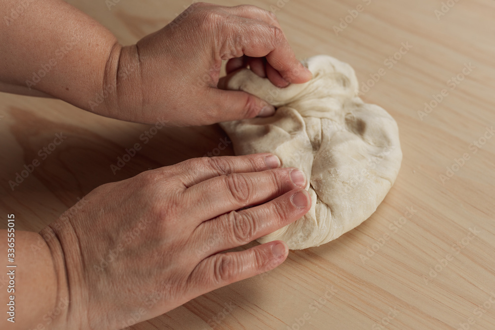 Overhead view of the hands of an adult woman kneading pizza dough in a wooden table in the kitchen Overhead view of the hands of an adult woman kneading pizza dough in a wooden table in the kitchen