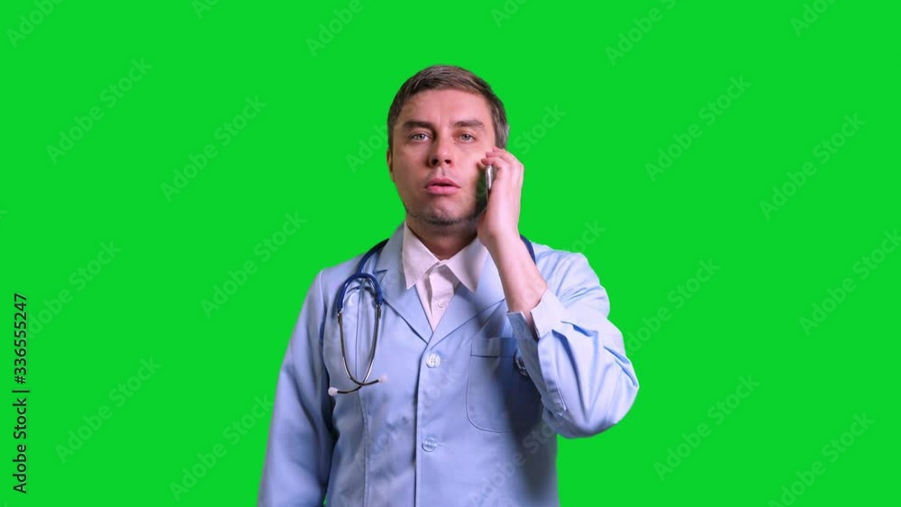 Young doctor using smartphone. Man in blue medical uniform with stethoscope on green chroma key background Young doctor using smartphone. Man in blue medical uniform with stethoscope on green chroma key background