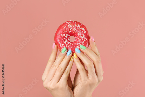 Hands of young woman with beautiful manicure and donut on color background