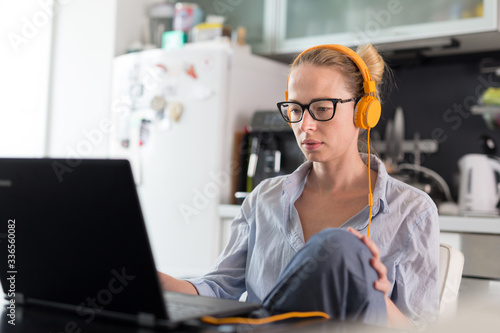 Female freelancer in her casual home clothing working remotly from her dining table in the morning. Home kitchen in the background. photo