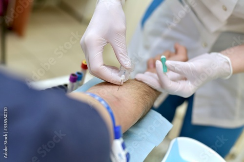  The process of taking venous blood through a needle for analysis in a patient of a male medical procedure nurse.
