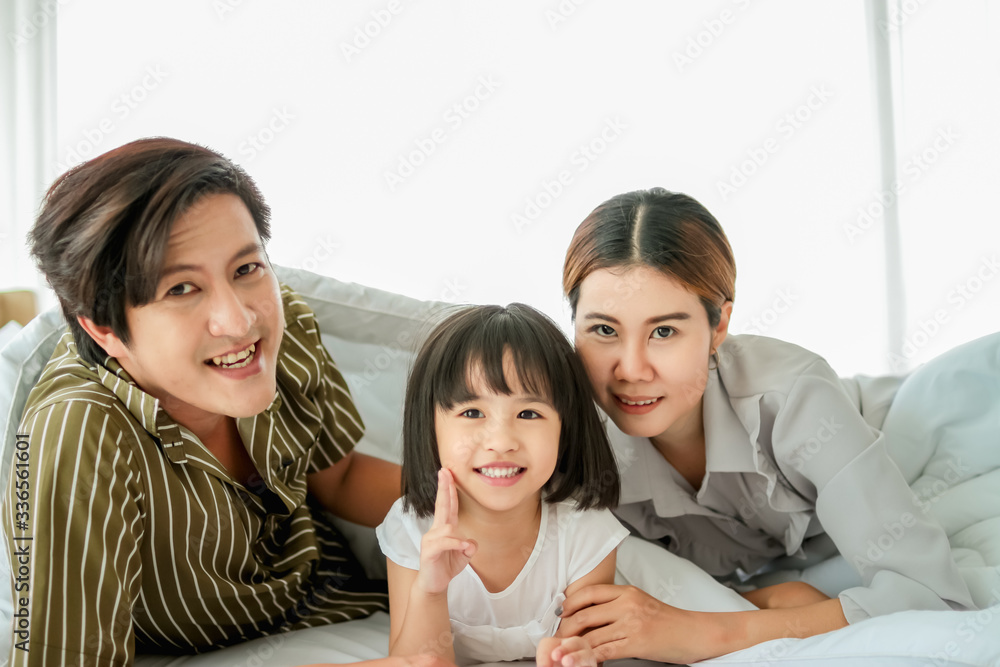 happy family having fun in bed room concept. father,mother and daugther smiling face, kiss love together lying on bed with duvet cover them copy space. happy family having fun in bed room concept. father,mother and daugther smiling face, kiss love together lying on bed with duvet cover them copy space.
