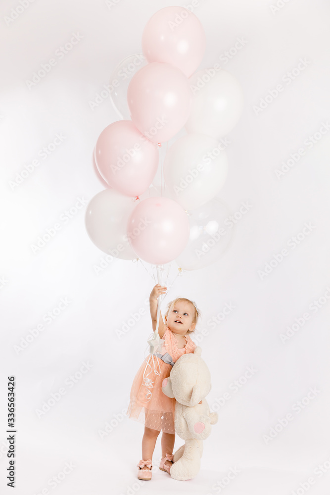 Little cute girl holds branch of balloons and large Teddy bear enjoy festive birthday event wear pink pastel summer dress isolated on a white background. Little cute girl holds branch of balloons and large Teddy bear enjoy festive birthday event wear pink pastel summer dress isolated on a white background.