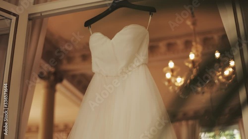 Beautiful tender white wedding dress is hanging on the window frame in the room, wedding preparation, bridal details