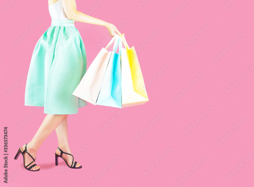 woman low body part wore blue skirt and black high heels. Carrying a shopping bag in many pastel colors on pink background selective focus