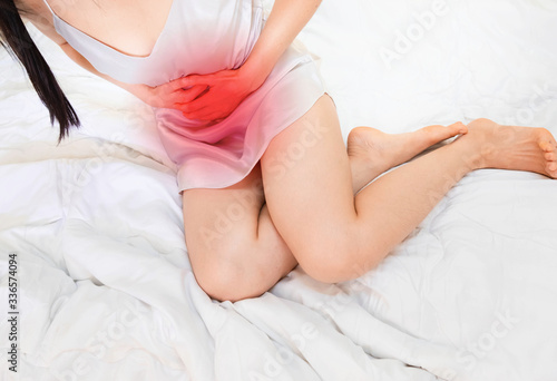 woman wearing white Sleepwear lying on bed stomachache .Acute Inflammation in a woman intestine holding hand to spot of belly-aches . Concept photo with read spot indicating location of the pain,