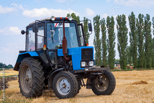 A tractor with a trailed bale making machine collects straw rolls in the field and makes round large bales