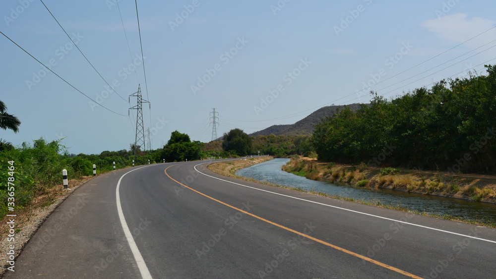 Irrigation and transportation system, Curve asphalt road along the canal with mountain and high voltage tower in Thailand Irrigation and transportation system, Curve asphalt road along the canal with mountain and high voltage tower in Thailand