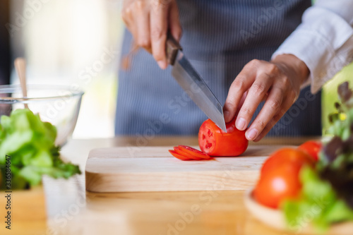 Closeup image of a woman chef cutting and chopping tomato by knife on wooden board