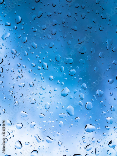 Rain drops on window glasses surface with blue cloudy background .