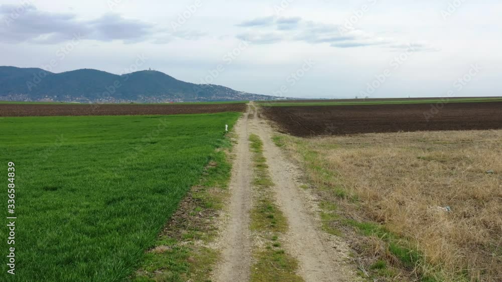 Low flight above a dirt road between agricultural fields with the hills in the background Low flight above a dirt road between agricultural fields with the hills in the background