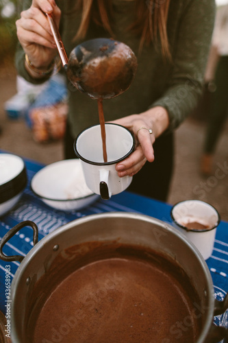 woman pouring hot chocolate into a camping mug outdoors