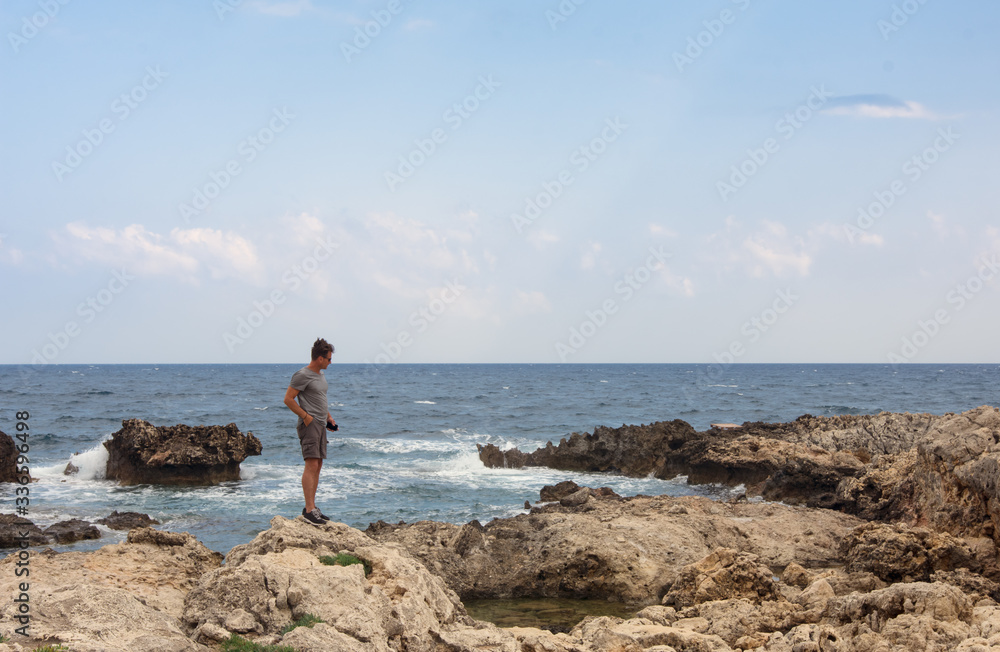 Adult man walks on the rocks from the shore of Greece, in summer vacation
