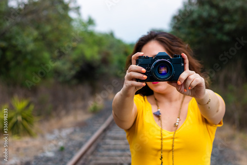 Real woman taking a selfie on the railroad track, in high heels, yellow dress and hat.