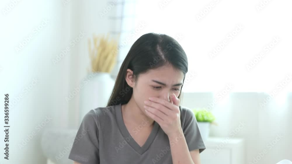 Beautiful young Asian woman in grey T-shirt in white bedroom coughing with torture face. Healthy, Coronavirus, covid-19, 2019-nCoV suspect and self quarantine concept Beautiful young Asian woman in grey T-shirt in white bedroom coughing with torture face. Healthy, Coronavirus, covid-19, 2019-nCoV suspect and self quarantine concept
