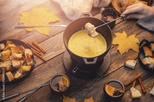 Girl cooks gourmet Swiss fondue dinner with cheese on fire, autumn wooden background with maple leaves. Top view, flat lay