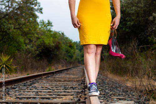 Detail of legs of a real woman walking on the railroad track, with heels, yellow dress and hat.