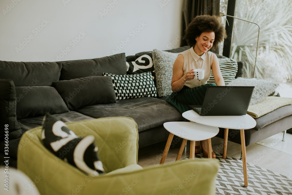 Young beautiful lady with curly hair work on the notebook while sit down on the couch at home Young beautiful lady with curly hair work on the notebook while sit down on the couch at home