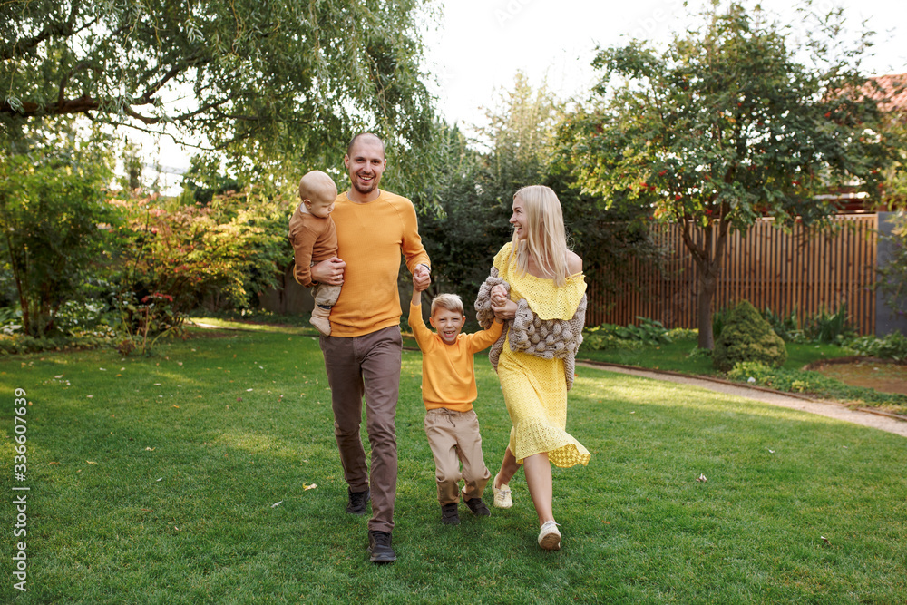 Obraz premium family in nature, summer or autumn, green grass trees in green leaves, a pond in nature, mom blonde in a yellow dress, dad, husband, older son and youngest son, two children, a large and happy family